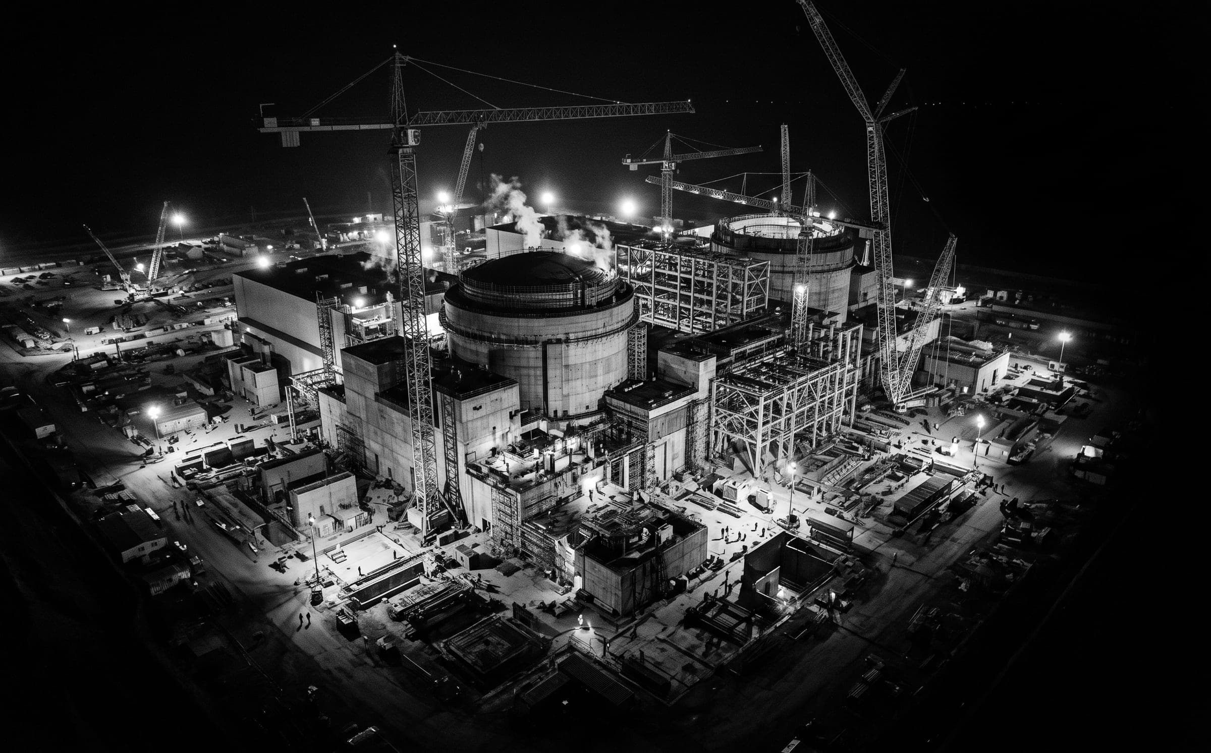 Vue aérienne de nuit d'un grand chantier industriel : grues, bâtiments en construction et éclairages.